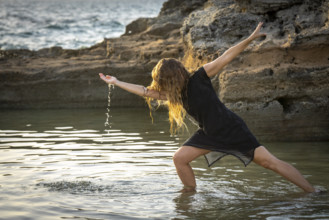 Middle-aged woman dancing and throwing water in the air, Maioris beach, llucmajor, Majorca,