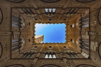 View into the sky of the Torre del Mangia, through a historic courtyard, Palazzo Pubblico, Siena,