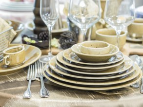 Set of new dishes on table with tablecloth. Stack of beige plates and wine glasses on restaurant