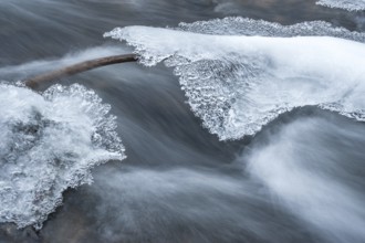 Long exposure in the current of a stream from a branch between two rocks covered with ice