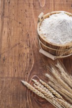 Flour in wooden bucket with ears of wheat on old table