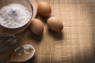 Three eggs flour in bowl empty spoon corolla on wooden board