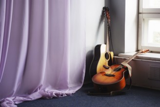Two acoustic guitar next the window and drapery