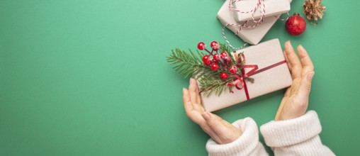 Christmas or New Year celebration green paper festive background with female hands holding wrapped