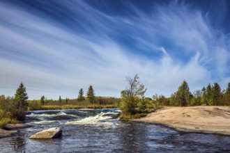 Foam water rapids on the smooth stones of the Winnipeg River. Thin cirrus clouds. Trend of travel