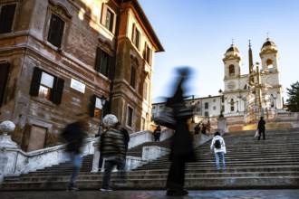 People in motion on the steps of the Spanish Steps in front of historic buildings under a blue sky,