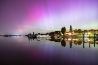 A calm lake at night, surrounded by shining auroras and reflecting houses, harbour, Allensbach,