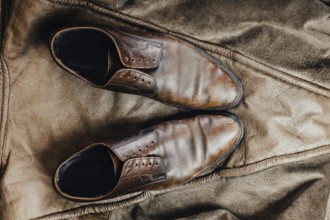 Overhead view of brown leather shoes on a rustic jacket, conveying a vintage feel