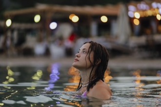 Woman in water gazing to the side, surrounded by colorful bokeh lights in the evening