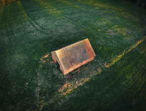 Hut in the evening light on a grass field, aerial view with long shadows at sunset, 27798