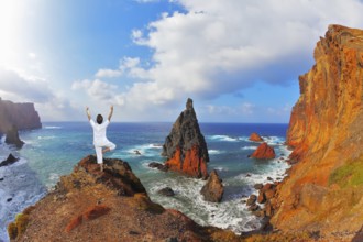 The woman ashore in a white suit for yoga carries out a pose Tree. Atlantic storms. Colorful