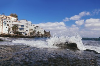 Sea wave with splashes and white houses near seashore at geek island