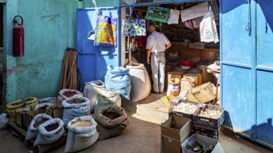 A man in a small shop full of colourful sacks and goods in bright sunshine, Small shop in