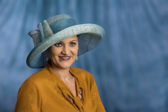 Woman wearing blue hat and yellow clothes, smiling in front of blue background, staged portrait