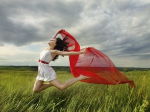 Brunette girl jumping with red fabric in summer day. Outdoors potrrait