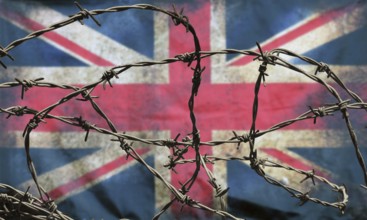 Barbed wire in front of an old stained dirty union jack british flag with dark crumpled edges