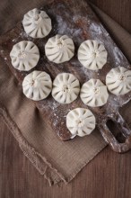 Freshly frozen khinkali, raw, on a wooden chopping board, top view, rustic style, no people