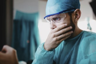 A surgeon in blue attire, appearing concerned with a hand on the mouth