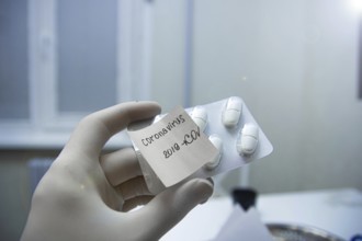 A gloved hand holds a pill package labeled 'Coronavirus 2019-nCoV' in a laboratory