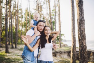 Family mom, dad and daughter sits at the daddy on the shoulders, and parents kiß on the nature in