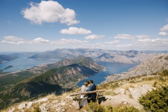 Bride and groom are sitting on a bench and looking at the Kotor bay. Excellent view from the