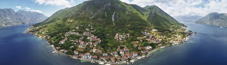Old houses with red roofs on the seashore on the slope of a green mountain. Montenegro. Drone.