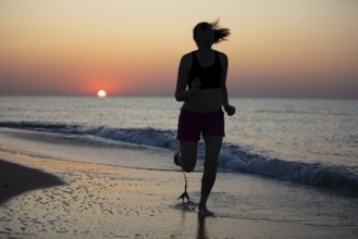 Silhouette of a sportswoman against the background of a sunrise by the sea