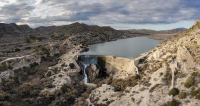 A drone view of the Elche Reservoir and dam wall with waterfall and surrounding semi-desert