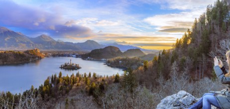 Panorama with the lake Bled under a colorful winter sky at sunrise and a young woman enjoys the