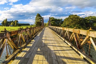 Wooden suspension bridge over a quiet river. South Island, New Zealand. Incredible cloudy sunset.