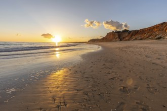 Beautiful sandy beach with red rocks and cliffs. Twilight at sunset with shallow waves on the