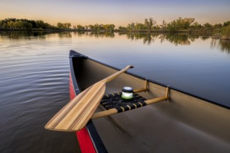 Red canoe with a wooden paddle and lantern on a lake at dusk, fall scenery, wide angle view