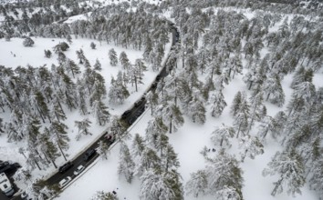 Drone aerial scenery of highway road crossing the snowy mountain forest landscape in winter.