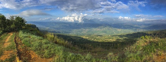 Panorama over the cliffs into a green valley and mountains in sun and shadow, blue sky and white