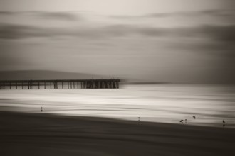 The smooth water of the Pacific with mountain silhouettes on the horizon and a wooden jetty