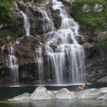 Professional model in elegant pose on a rocky island in front of an impressive waterfall, Aesthetic