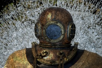 Metal diving helmet with round viewing windows amidst swirling air bubbles. Landscape format.