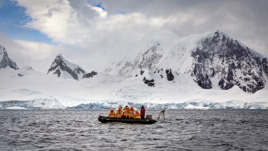 Group in a boat in the foreground, surrounded by snow-covered mountains and overcast sky, people in