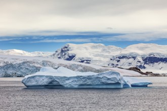 A large iceberg floats in the sea, surrounded by snowy mountains under a blue sky, iceberg in the