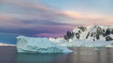 Iceberg floating in the sea in front of a snow-covered mountain backdrop at sunset, icebergs in the