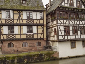 Two historic half-timbered houses side by side along a canal on a rainy day, strasbourg, france