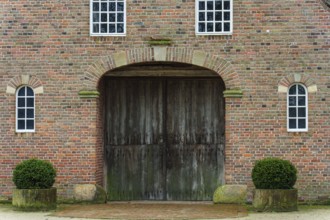 Large wooden gate in a symmetrical brick building with trimmed shrubs, vreden, münsterland, North