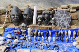Various masks and sculptures displayed on a market stall with a blue ceiling, at the Tichka Pass,