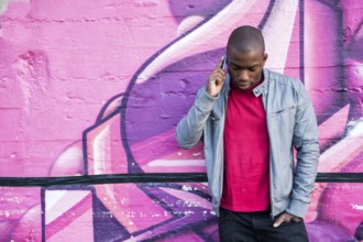 Portrait of a hot black man in front of graffiti wall, using cell phone, posing for camera