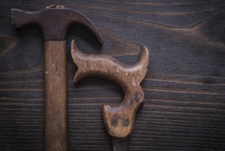 Rusted messy handsaw and claw hammer on vintage wooden background