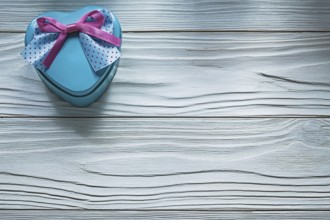 Heart-shaped blue present box with pink bow on wooden board holidays concept