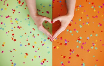 Top view of anonymous female with hands in shape of heart on two colored background with confetti