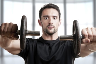 Personal Trainer doing front dumbell raises for training his deltoids in a brown background