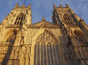 A front view of the towers at the entrance to york minster in sunlight against a blue cloudy sky