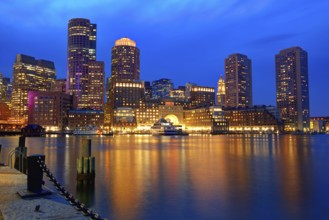 Boston\'s skyline glows at sunset, reflecting off the water at Fan Pier.